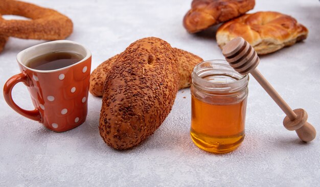 Vista lateral de deliciosas empanadas de sésamo con una taza de té y miel en un frasco de vidrio sobre un fondo blanco.