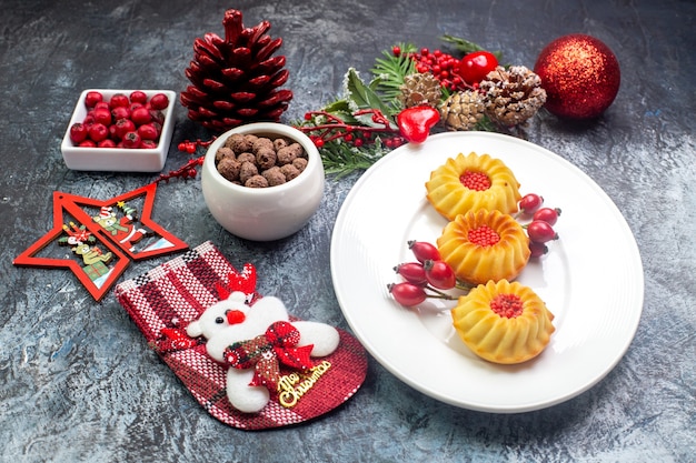 Vista lateral de deliciosas galletas en un plato blanco santa claus sock y cornell en un tazón de ramas de abeto sobre superficie oscura