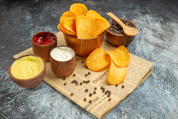 Vista lateral de deliciosas patatas fritas caseras y salsa de tomate mayonesa tazón de pimienta y salsa con una cuchara en el periódico sobre la mesa gris