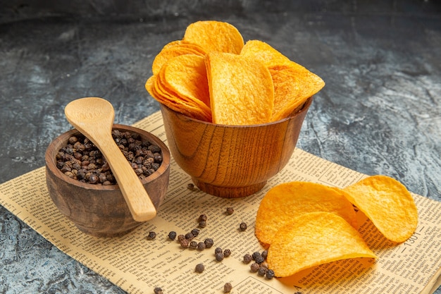 Vista lateral de deliciosas patatas fritas caseras y tazón de pimienta con una cuchara de periódico en la mesa gris