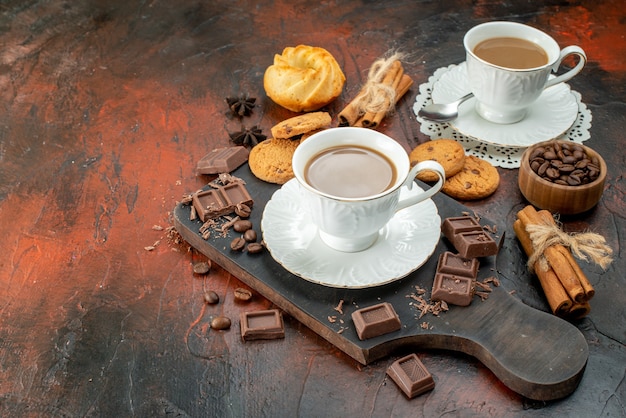 Vista lateral del delicioso café en tazas blancas en la tabla de cortar de madera galletas canela limas barras de chocolate en el lado izquierdo sobre fondo de color mezclado