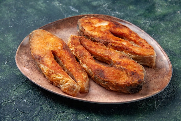 Vista lateral de un delicioso pescado frito en una placa marrón en el lado izquierdo en la mesa de mezcla de colores con espacio libre
