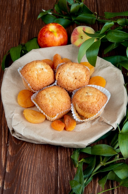 Vista lateral de deliciosos muffins y albaricoques secos en un plato y nectarinas dulces frescas en la mesa rústica de madera