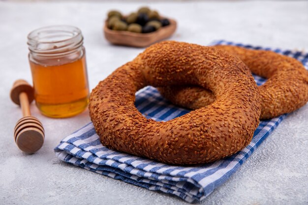 Vista lateral de deliciosos y suaves bagels turcos tradicionales aislados en una tela marcada con miel y cuchara de miel sobre un fondo blanco.