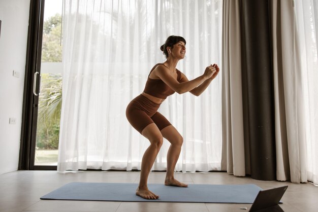 La vista lateral de la deportista haciendo ejercicio en casa en karamet en la computadora portátil