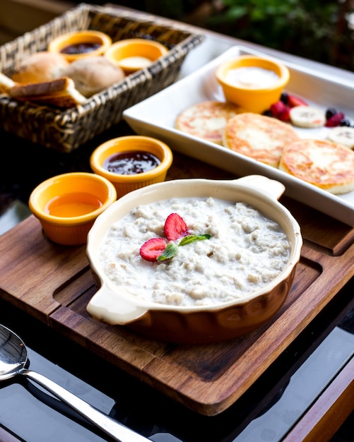 Vista lateral desayuno conjunto de avena con mermelada de miel de fresa panqueques de queso bayas y plátano en una bandeja