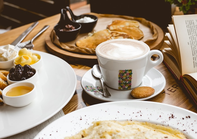 Vista lateral desayuno taza de capuchino con aperitivos y panqueques con mermelada