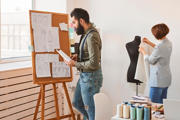 Vista lateral de diseñadores de moda en taller con forma de vestido y tablero de ideas