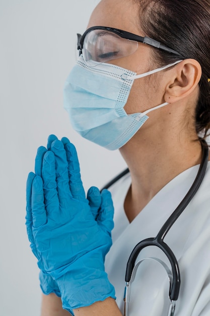 Foto gratuita vista lateral de la doctora con máscara médica y guantes rezando