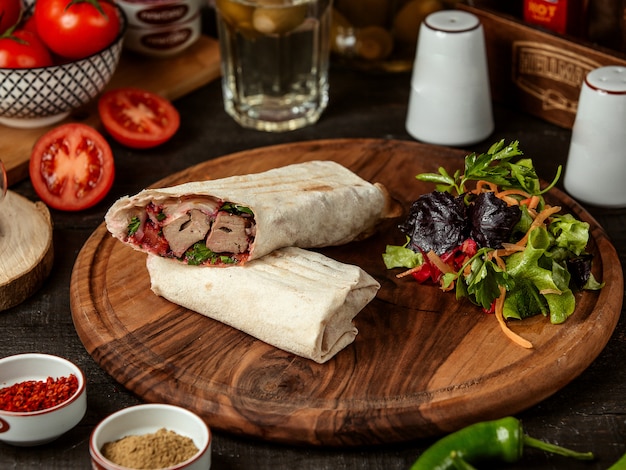 Vista lateral del doner kebab envuelto en lavash con ensalada fresca sobre tabla de madera