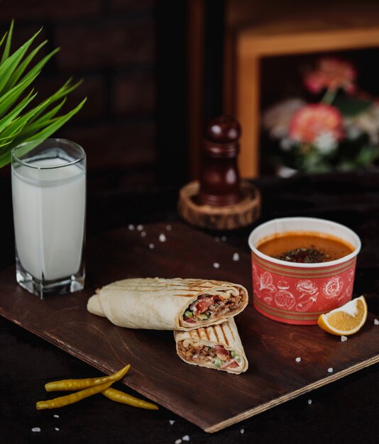 Vista lateral de doner de pollo envuelto en lavash servido con lentejas merci sopa y bebida ayran en una tabla de madera