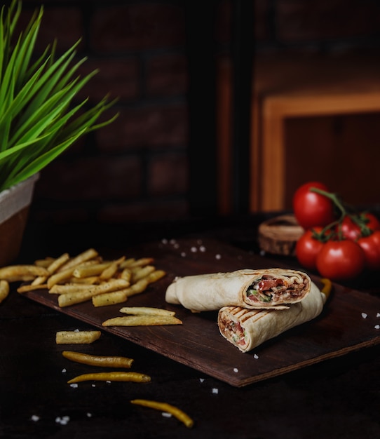 Vista lateral de doner de pollo envuelto en papas fritas y lavash sobre una tabla para cortar madera