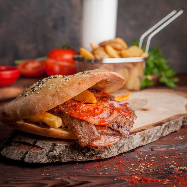 Vista lateral doner con tomate y papas fritas y pan en utensilios de cocina