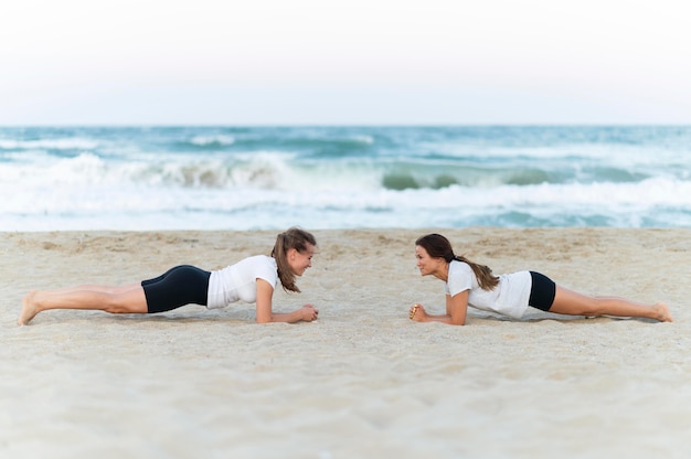 Foto gratuita vista lateral de dos amigas haciendo ejercicio en la playa