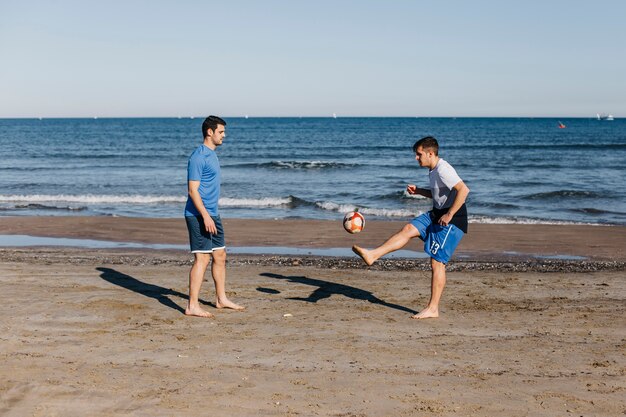 Vista lateral de dos amigos jugando al fútbol en la playa