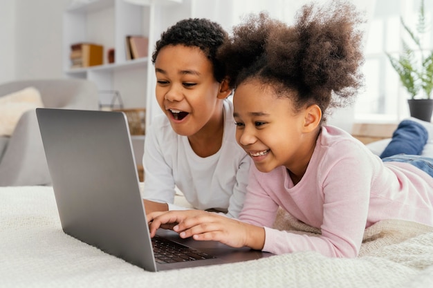 Vista lateral de dos hermanos en casa juntos jugando en la computadora portátil