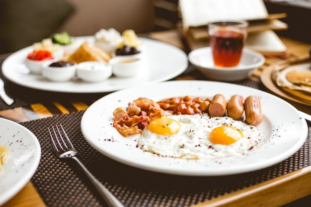 Vista lateral dos huevos fritos con salchichas frijoles y tocino en un plato