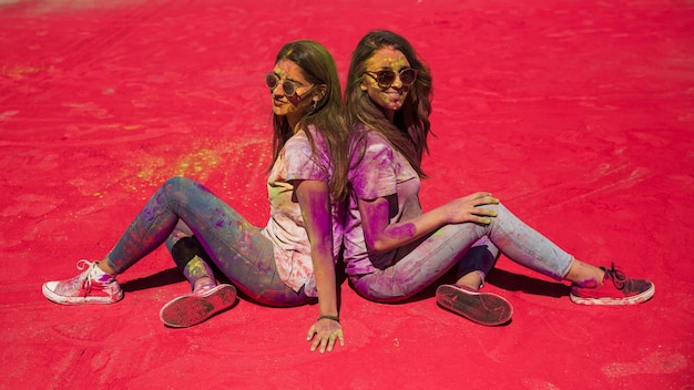 Foto gratuita vista lateral de dos mujeres jóvenes sentadas espalda con espalda con color holi