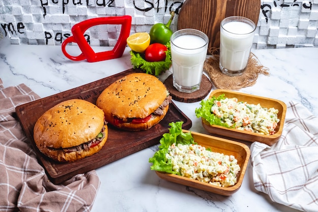 Vista lateral dos porciones de carne doner en pan con dos porciones de ensalada capital y dos vasos de yogurt