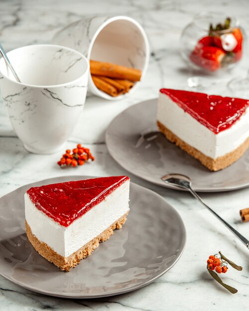 Vista lateral dos tarta de queso de fresa con una taza de té y canela