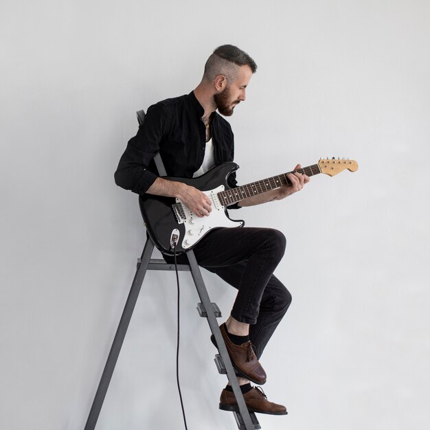 Vista lateral del ejecutante masculino tocando la guitarra eléctrica en las escaleras