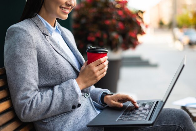 Foto gratuita vista lateral de la empresaria sosteniendo una taza de café mientras usa la computadora portátil