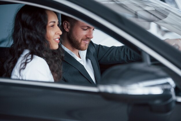 Vista lateral. Encantadora pareja exitosa probando coche nuevo en el salón del automóvil