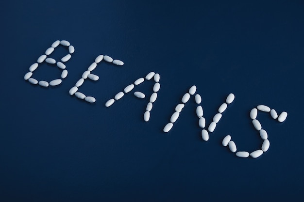 Vista lateral enfocada palabra frijoles con letras con montón de frijoles blancos aislado en la superficie de la mesa azul rústico