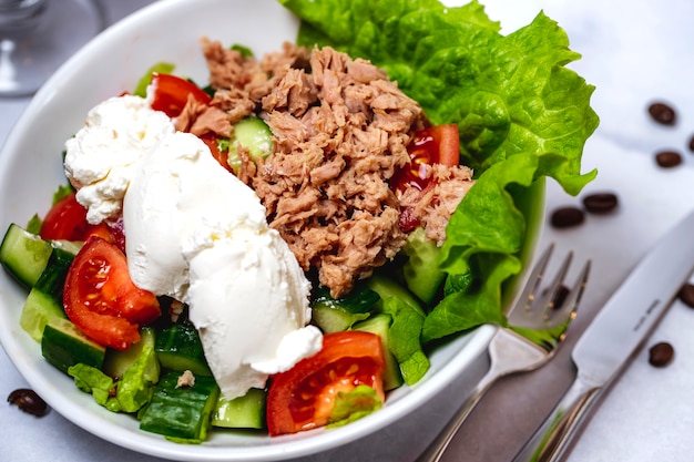 Vista lateral ensalada de atún con lechuga tomate pepino y crema agria en un plato