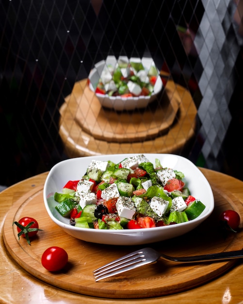 Vista lateral de ensalada fresca con queso feta, tomates, pepinos y hierbas secas con aceite de oliva en un tazón blanco