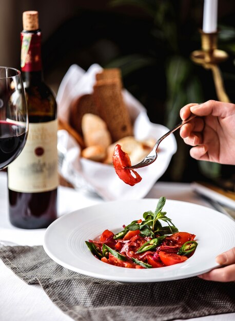 Vista lateral de ensalada fresca con tomate, pimiento verde, cebolla roja y salsa de granada en un tazón blanco