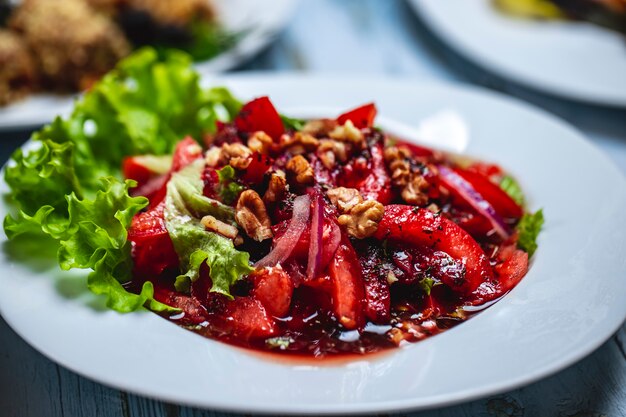 Vista lateral ensalada georgiana con rodajas de tomate cebolla roja nuez salsa de ciruelas y lechuga en un plato