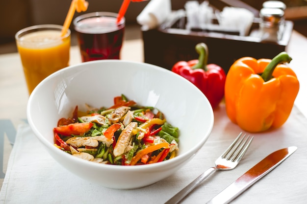 Vista lateral ensalada de pollo con pimiento tomate pepino lechuga de pollo a la parrilla y refrescos en la mesa