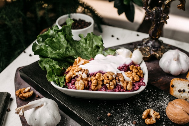 Vista lateral de ensalada de remolacha con nueces y crema agria en una tabla de madera