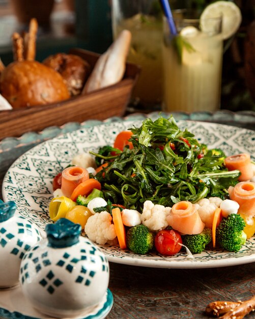 Vista lateral de ensalada de salmón ahumado con verduras y rúcula en un plato sobre la mesa