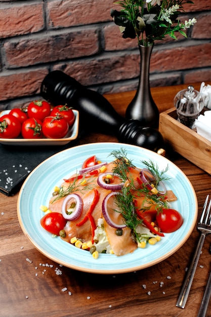 Vista lateral de ensalada de salmón con cebolla roja, repollo y callos cubiertos con eneldo en plato sobre mesa de madera