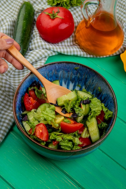 Vista lateral de ensalada de verduras con tomate pepino sobre tela y mesa verde