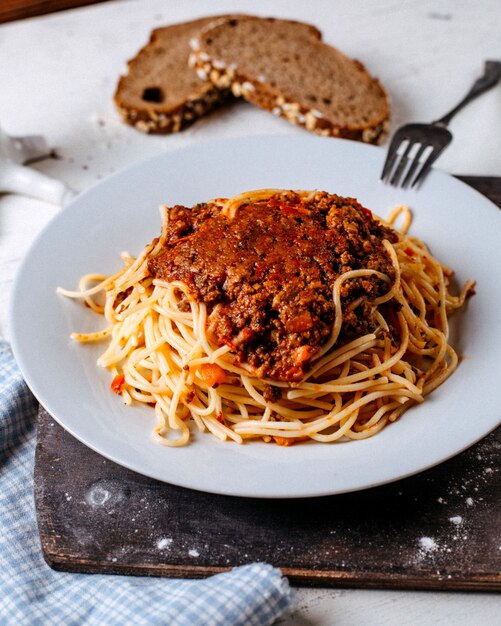 Vista lateral de espaguetis a la boloñesa en plato blanco