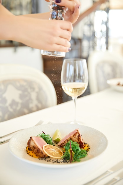 Vista lateral de espolvorear con especias un plato de atún con una copa de vino blanco en el restaurante