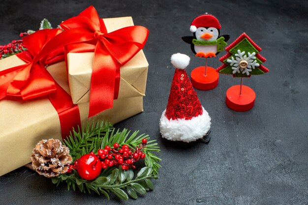 Vista lateral del estado de ánimo navideño con hermosos regalos con cinta en forma de arco y accesorios de decoración de ramas de abeto sombrero de santa claus conos de coníferas sobre un fondo oscuro