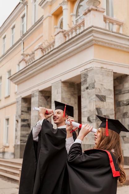 Foto gratuita vista lateral de los estudiantes que usan el diploma como binocular