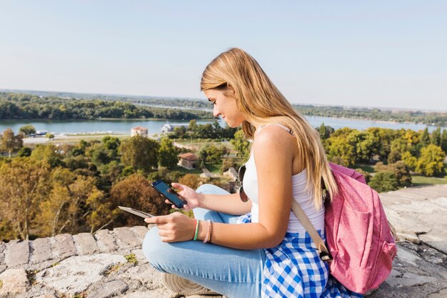 Vista lateral de un excursionista femenino usando un teléfono celular al aire libre