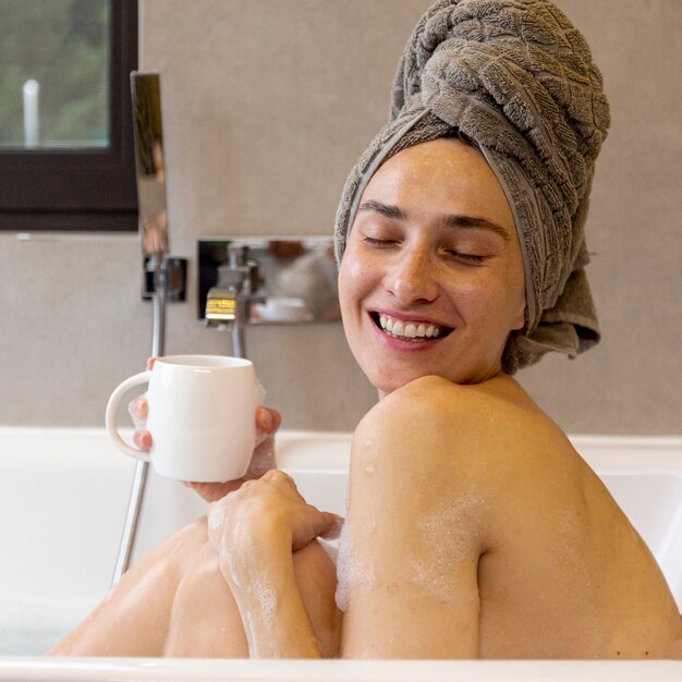 Vista lateral feliz mujer con taza en la bañera