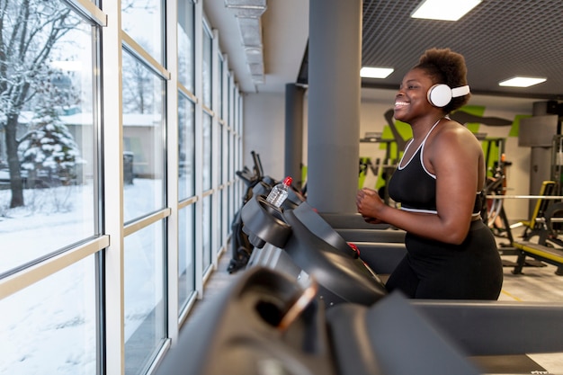 Vista lateral femenina en el gimnasio corriendo en cinta