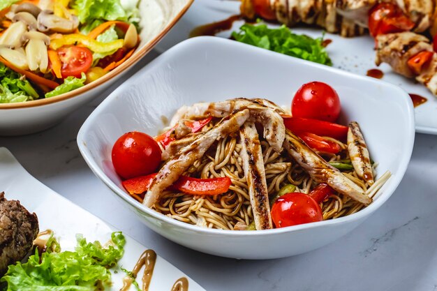 Vista lateral fideos fritos con salsa pimiento pollo a la parrilla y tomate en un plato