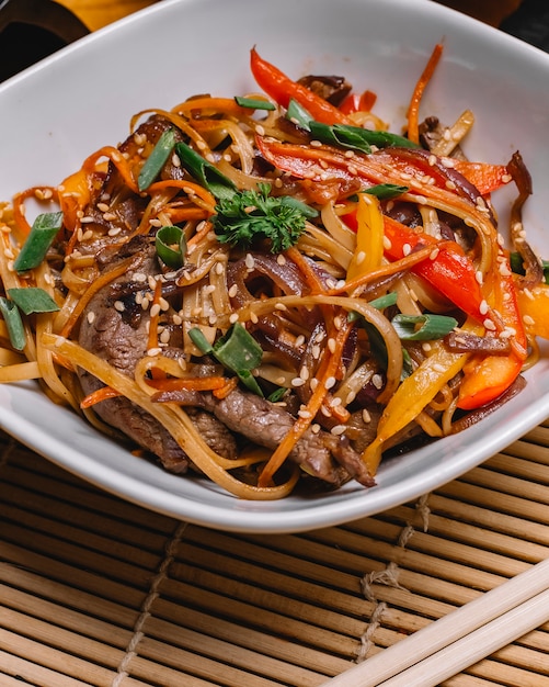 Foto gratuita vista lateral fideos salteados con carne a la parrilla, pimientos, cebolla tierna y semillas de sésamo