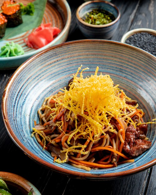 Vista lateral de fideos salteados con carne y verduras en un plato sobre la mesa de madera