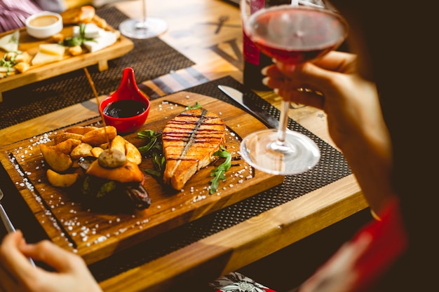 Vista lateral filete de salmón con patata en una salsa de granada rural sal y copa de vino sobre la mesa