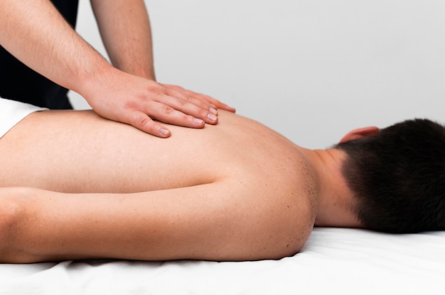 Vista lateral del fisioterapeuta masajeando la espalda del hombre.