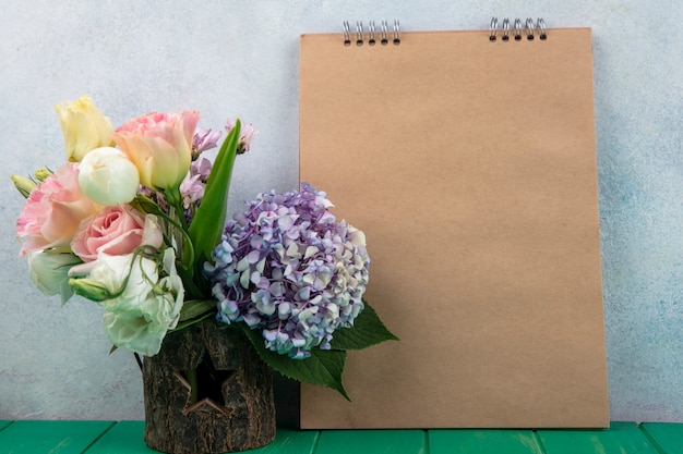 Foto gratuita vista lateral de flores en un tazón de árbol y bloc de notas sobre una superficie verde y fondo blanco con espacio de copia